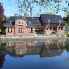 Stort, rødt hus ligger ud til noget vand og spejler sig flot i det. 