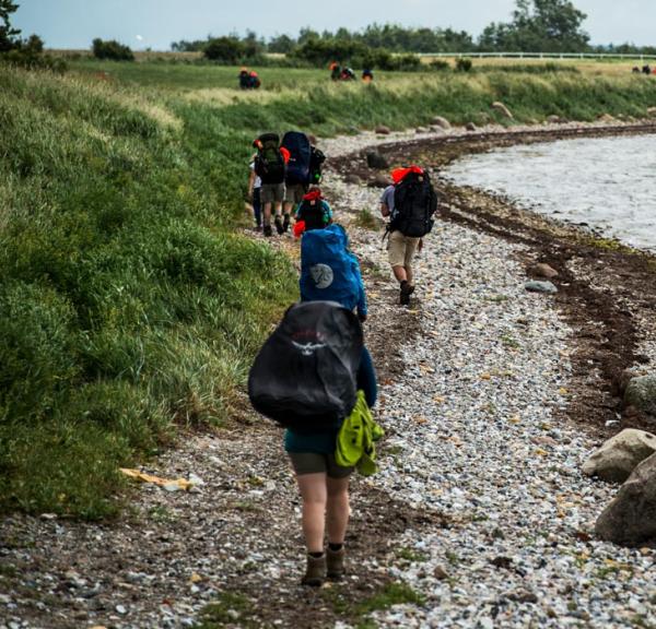 Fire vandrere med oppakning og sommertøj på en stenstrand ned til havet. 