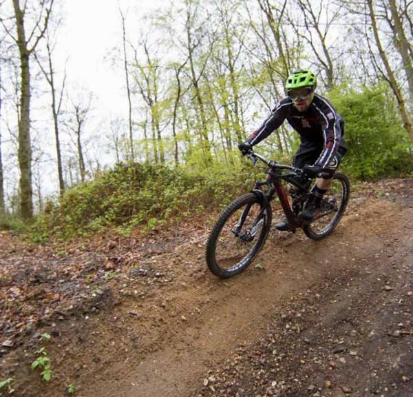 En mountainbiker med grøn hjelm cykler i skoven på vej ned ad en bakke.