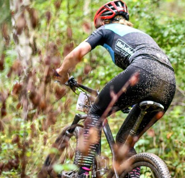 Mountainbiker med rød hjelm er til løb og cykler ude i skoven omringet af en masse grønt.