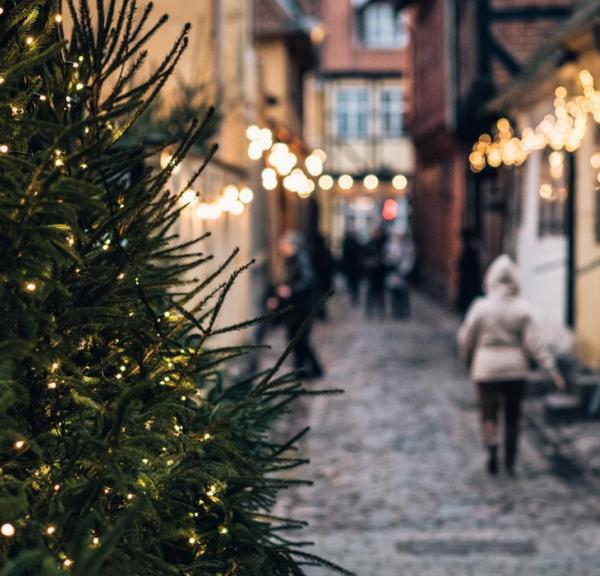 I højre side står et juletræ med julelys. Bag juletræet ses en sløret brostensgade der går ned mellem to rækker af gamle bindingsværkshuse. På husene hænger julelys, og på gaden går et par mennesker.
