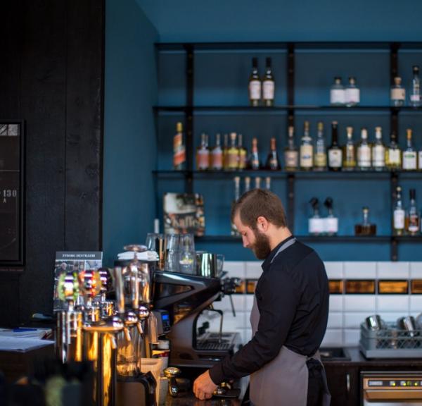 En mandlig barista står bag baren på en restaurant.