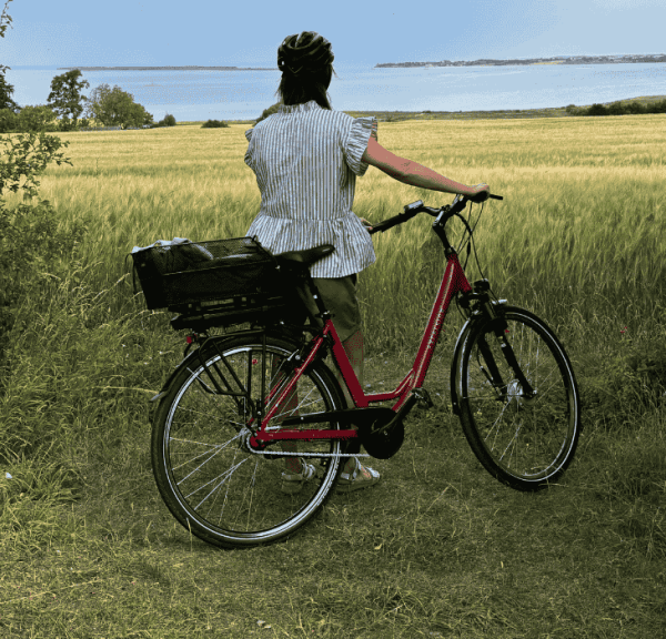 En cyklist står ved siden af en cykel og kigger ud over en mark med havet i horisonten