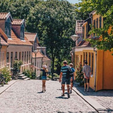 Fire personer i sommertøj ses gående ned ad Paaskestræde i Odense. Det er sommer og solen skinner.