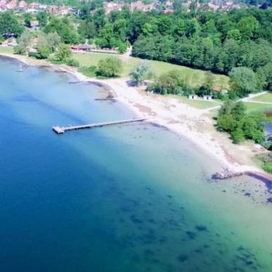 Strand set ovenfra med lyst sand og blåt og turkis vand.