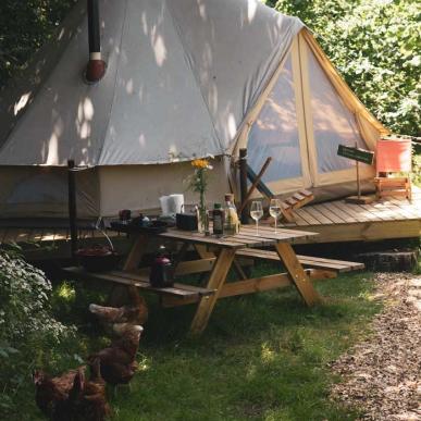 Glampingtelt i grønne omgivelser med et bål tændt ude foran.
