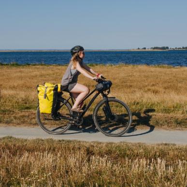 Kvindelig cyklist med oppakning og cykelhjelm på sti ud til havet om sommeren.