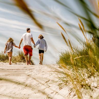 En familie går hånd i hånd på en strand.