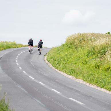 To cyklister på vej op ad bakke på landevej med grønt omkring. 