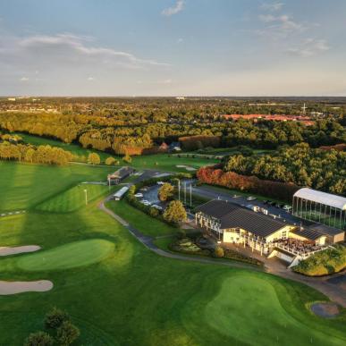 Udsigt over grøn golfbane oppefra med golfklubbens lokaler i forgrunden og Odense by i baggerunden.