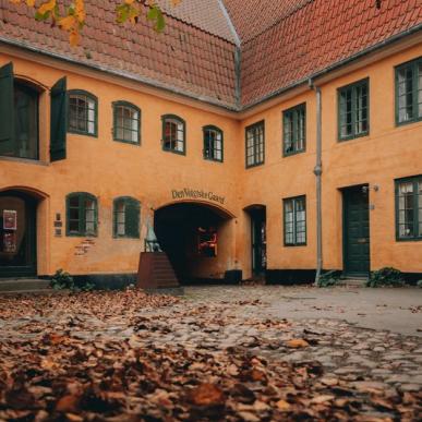 En gulmalet ældre bygning i efteråret med gule og orange blade i gårdhaven