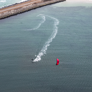En kitesurfer med rødt sejl driver på stille vand ud for en dæmning