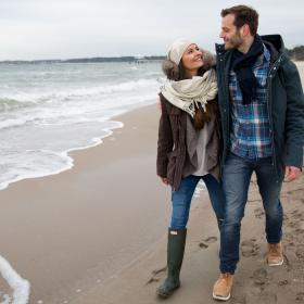 Par går langs vandkanten på stranden i tykt overtøj da det er vinter