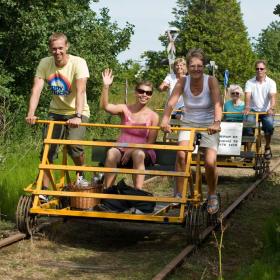 En flok mennesker kommer kørende på to skinnecykler og smiler og vinker til kameraet.