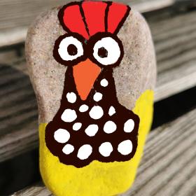 Close-up af en sten, hvor der er malet en høne på i gule, røde, orange, sorte og hvide farver.