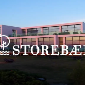 Hvidt hotel med store vinduer, der afspejler en solnedgang. Logo og teksten "Storebælt"