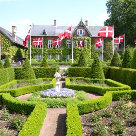 Prinsesse Maries have, Humlemagasinet. Fransk parterrehave med taks, buksbom og berleburgroser med hus og danebrosflag i baggrunden.