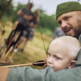 Et barn får undervisning i bueskydning af en vikingeklædt mand