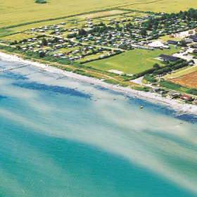 Luftfoto af Camp Hverringe, som ligger omkranset af marker lige ud til en hvid og lavvandet strand