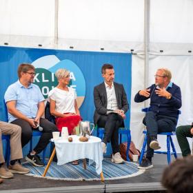 6 paneldeltagere sidder på lille scene i telt og debatterer ved Klimafolkemødet 2024.