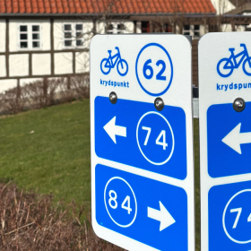 Cykelnetskilte på Langeland med bindingsværkshus i baggrunden