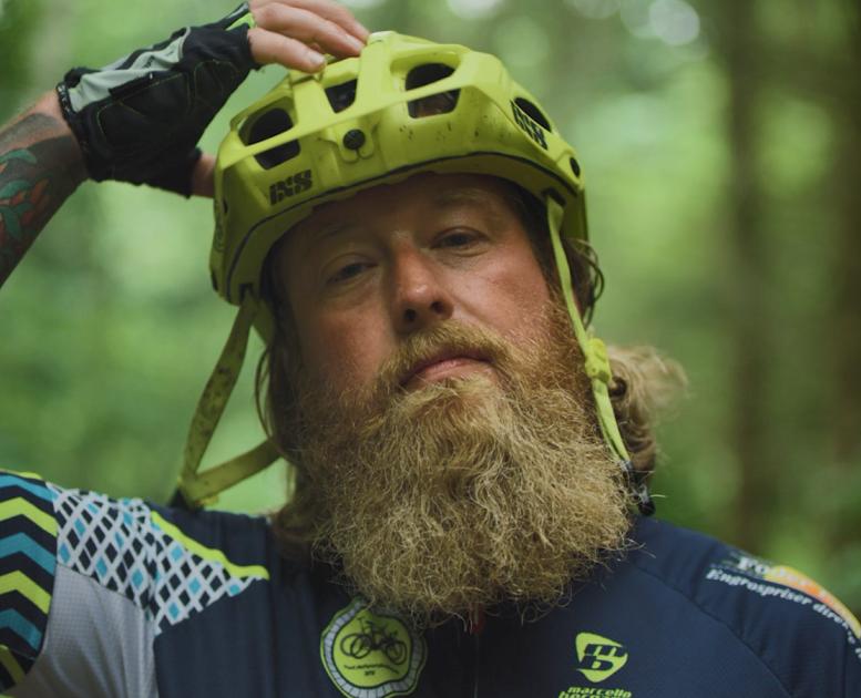 Close-up af mand med fuldskæg og tatoveringer på armen, der sætter cykelhjelmen på hovedet.