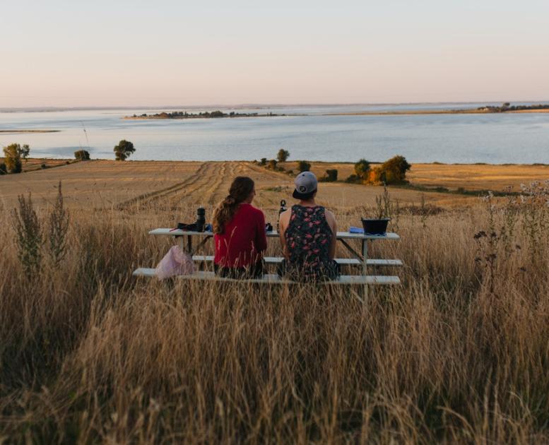 På en mark med udsigt udover havet står et bordebænkesæt. På bænken sidder to kvinder og kigger udover vandet.