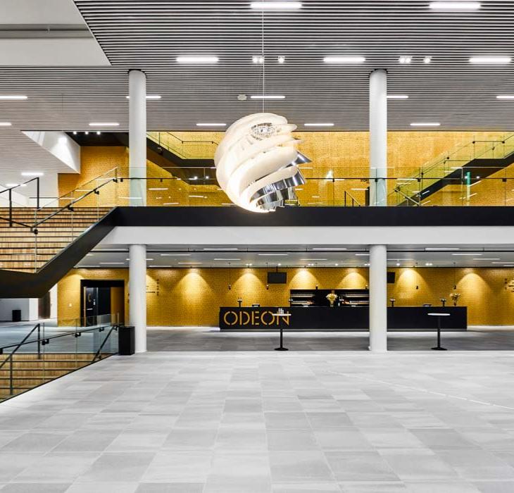 Stor, tom sal i Odeon, hvor man kan se, etagen overover også. Der er trapper i venstre og højre side af salen og en stor, rund lampe hænger ned i midten af billedet og oplyser salen.