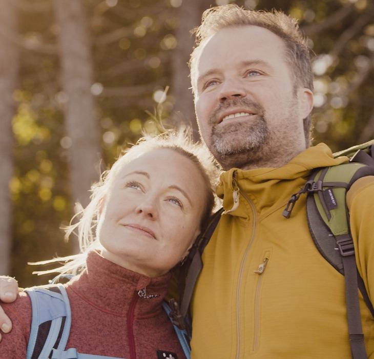 Closeup af kvinde og mand, der holder om hinanden med skov i baggrunden og sol i ansigterne.