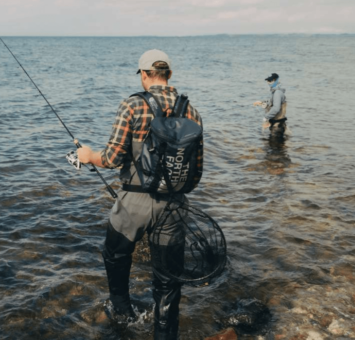 To lystfiskeri iklædt outdoortøj og waders står i havet med fiskestænger